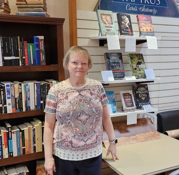 Linda Grana in front of shelves with books and Linda's reviews of them.
